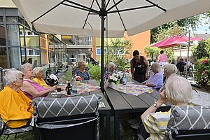 Gruppe älterer Menschen sitzt an einem Gartentisch unter einem großen Sonnenschirm im Freien