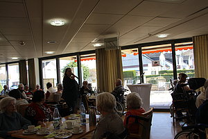 Veranstaltung in einem Seniorenheim mit Gästen am Tisch und einer Person, die spricht.
