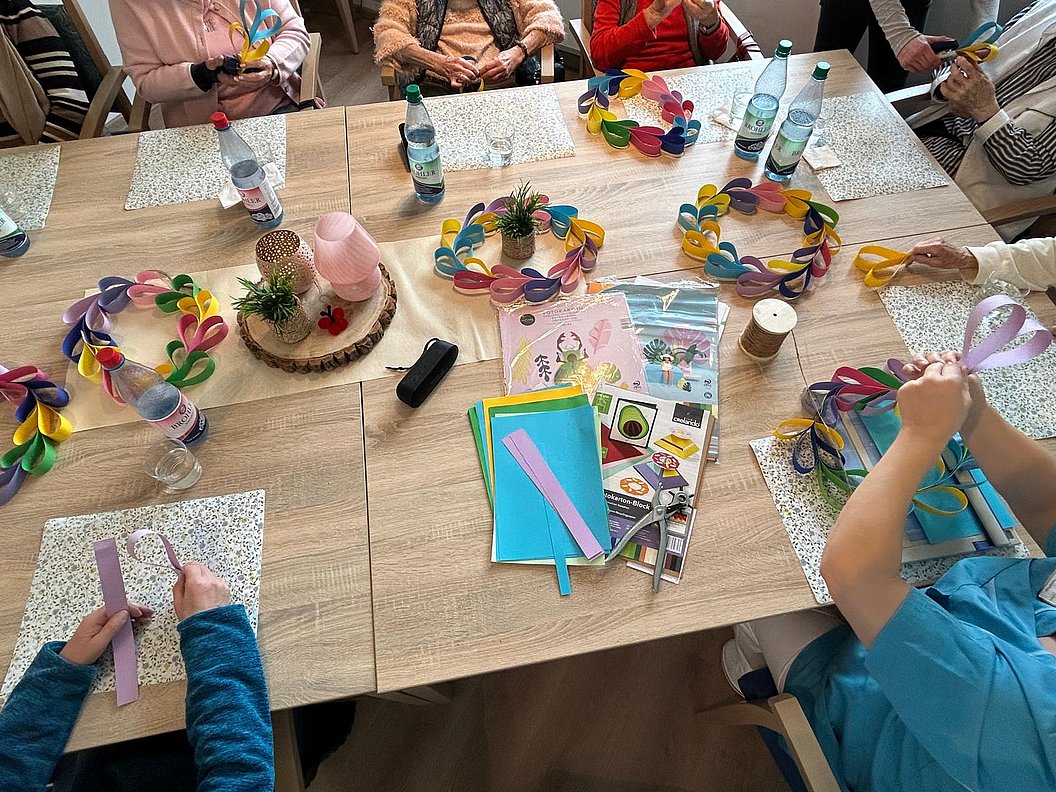 Kreatives Basteln am Tisch mit bunten Papierkränzen und verschiedenen Bastelmaterialien.