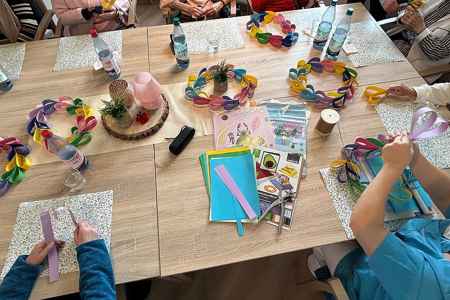 Kreatives Basteln am Tisch mit bunten Papierkränzen und verschiedenen Bastelmaterialien.