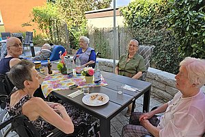 Gruppe älterer Menschen sitzt an einem Gartentisch mit Getränken und Snacks