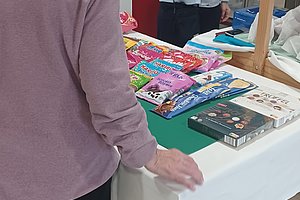 Zwei Frauen an einem Tisch mit bunten Stoffen und Materialien in einer Verkaufsumgebung.