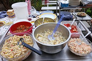 Mehrere Schüsseln mit verschiedenen Salaten und Speisen auf einem Tisch im Freien