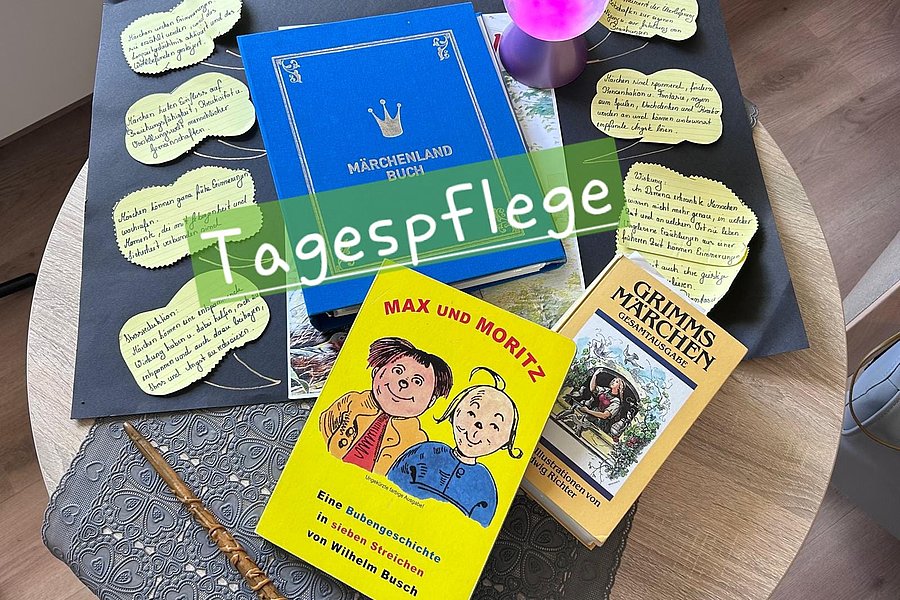 Auf einem runden Tisch liegen drei Bücher, darunter ein gelbes "Max und Moritz"-Buch, ein blaues "Märchenland Buch" und ein "Grimms Märchen"-Buch, umgeben von mehreren handgeschriebenen Notizzetteln und einer kleinen pink leuchtenden Lampe.