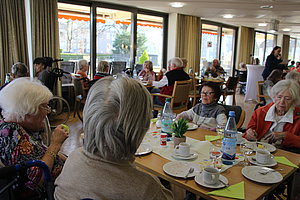 Geselliges Beisammensein in einer Einrichtung mit Seniorinnen und Senioren bei Kaffee und Kuchen.