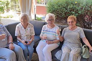 Vier Frauen in bequemen Outfits sitzen auf einer Couch und stoßen mit Gläsern an.