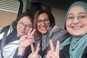 Drei Frauen im Auto, lächelnd und mit Peace-Zeichen, fröhliche Stimmung.