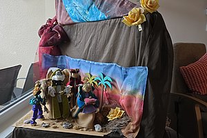 Kleine Figuren und Dekorationen auf einem Tisch vor einem mit Tüchern bedeckten Stuhl in einem Wohnzimmer