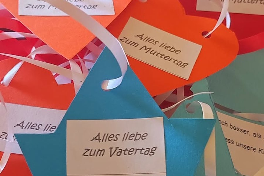 Bunte Geschenkanhänger in Form von Booten, mit Sprüchen zum Mutter- und Vatertag.
