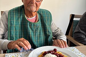 Älterer Mann sitzt an einem Tisch mit Teller, auf dem Waffeln mit Sahne und Kirschen angerichtet sind