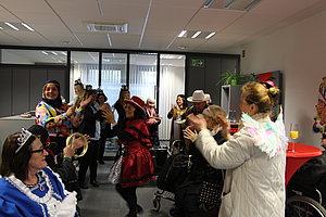 Menschen in farbenfrohen Kostümen klatschen und tanzen in einem Büro mit Glaswänden und Pflanzen