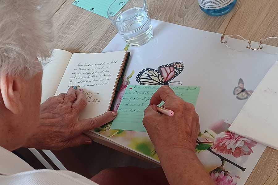Person sitzt an einem Tisch und zeichnet einen Schmetterling in ein Buch