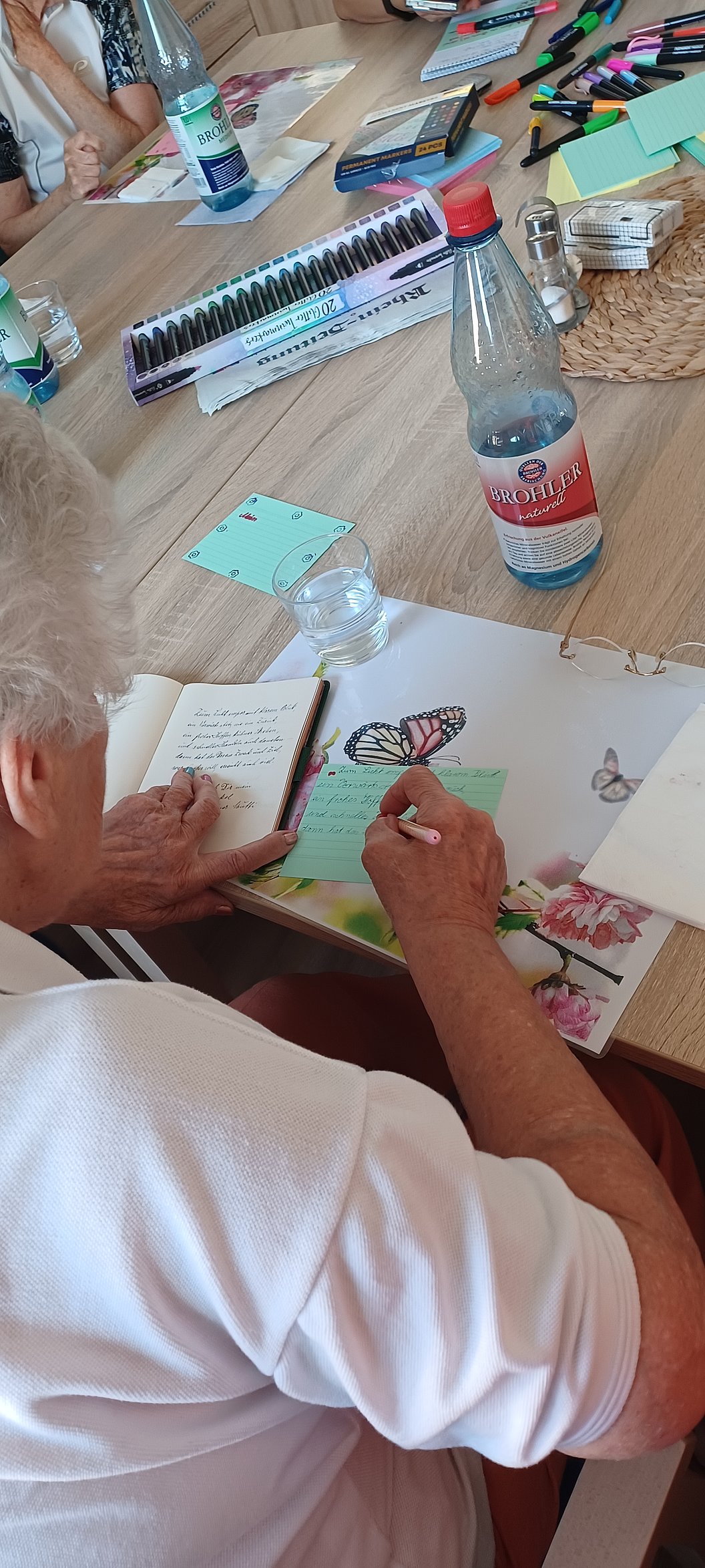 Person sitzt an einem Tisch und zeichnet einen Schmetterling in ein Buch