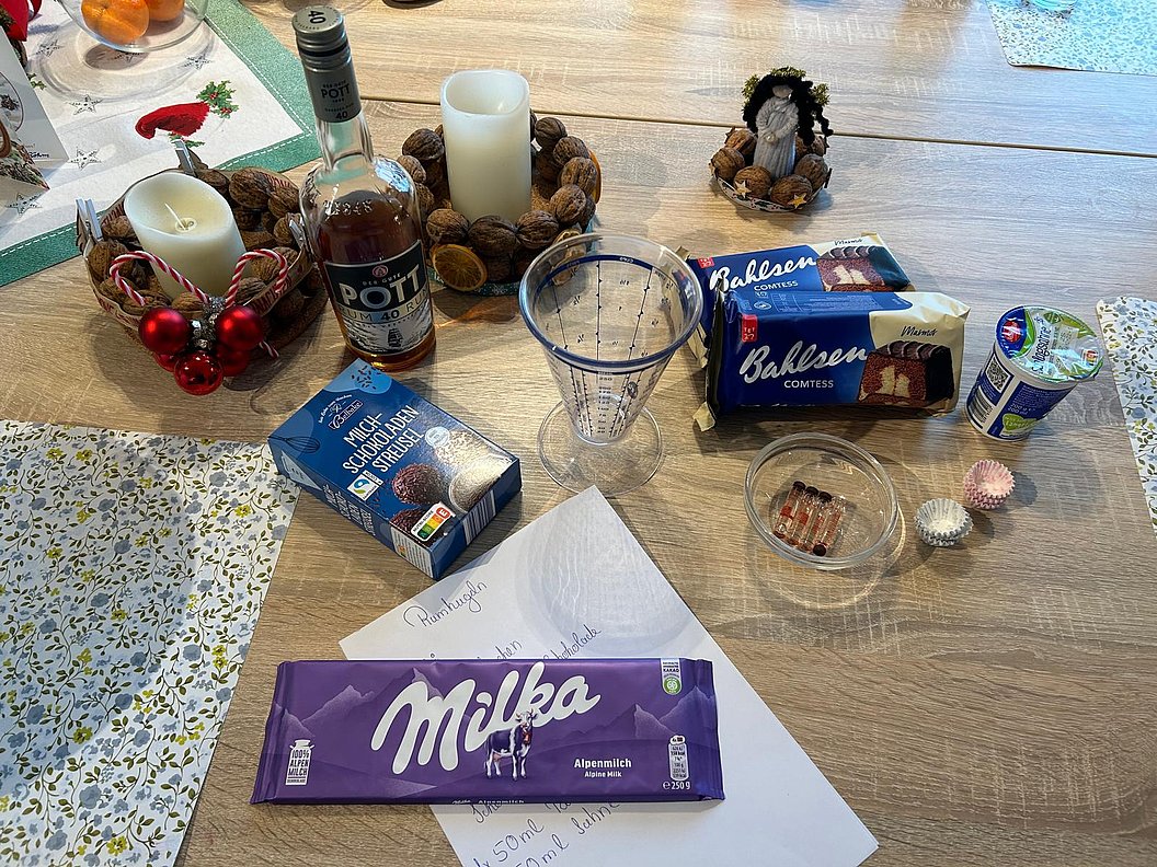Tischdekoration mit Milka Schokolade, Getränken, Kerzen und Weihnachtsgebäck auf einem holzfarbenen Tisch.