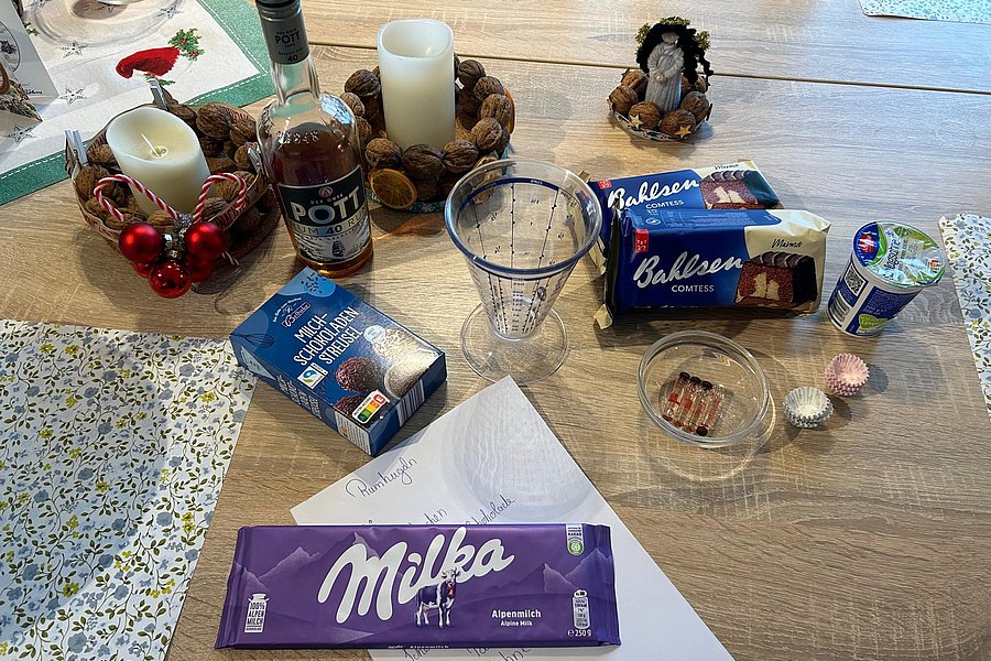 Tischdekoration mit Milka Schokolade, Getränken, Kerzen und Weihnachtsgebäck auf einem holzfarbenen Tisch.