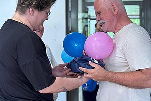 Zwei Personen stehen sich gegenüber und halten gemeinsam bunte Luftballons