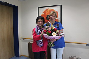 Zwei Frauen posieren mit einem großen Blumenstrauß vor einem Blumenbild.