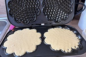 Offener Waffeleisen mit zwei ungebackenen, blütenförmigen Teigportionen