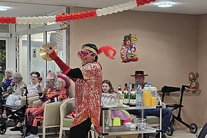 Tanzende Person in bunter Kostümierung mit Zimbeln vor Zuschauern in einem festlichen Raum.