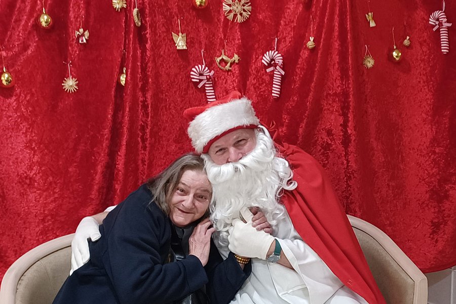 Frau und Weihnachtsmann auf einer Couch vor rotem Hintergrund mit Weihnachtsdeko.