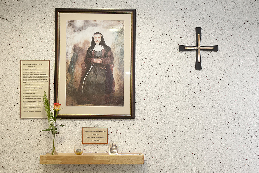 Wanddekoration mit einem portraitierten Bild unserer Mutter Rosa Flesch, einer Blume und einer Holzregal mit Tafel.