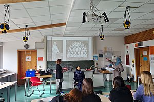 Lernsituation in einem Klassenzimmer mit Präsentation und Schülern am Tisch.