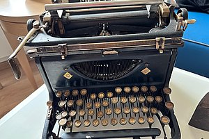 Schwarze mechanische Schreibmaschine mit runden Tasten auf einem weißen Tisch