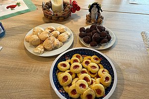 Drei Teller mit verschiedenen Keksen auf einem Holztisch, im Hintergrund eine Kerze in einem Korb und eine kleine Weihnachtsdekoration