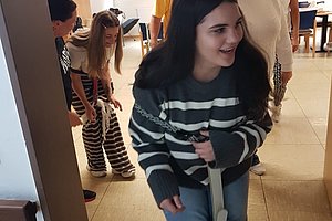 Gruppe von Menschen in einem hellen Raum, eine Person im Vordergrund hält ein Seil, andere stehen oder bücken sich im Hintergrund