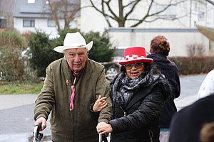 Paar mit einem weißen und roten Hut beim Spazierengehen auf der Straße, freundlich miteinander interagierend.