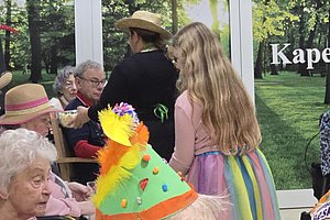 Bunte Feier mit Senioren in einem Gemeinschaftsraum, inkl. Partyhut und fröhlicher Kostüme.