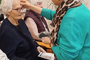 Eine ältere Dame sitzt in einem Sessel, während eine Betreuerin ihm freundlich die Haare strich.