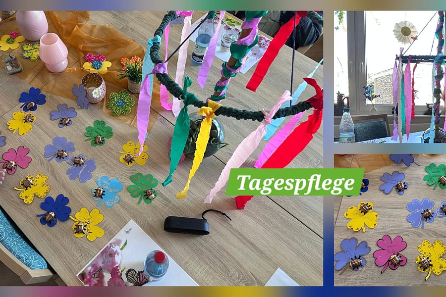 Kinder basteln bunte Papierblumen auf einem Holztisch und hängen bunte Bänder an eine grüne Girlande in einem hellen Raum