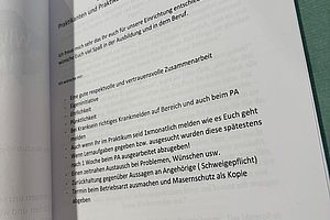 Blatt mit gedrucktem Text in deutscher Sprache, das an einer Pinnwand mit blauem Magneten befestigt ist