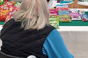 Person im Rollstuhl blickt auf einen Tisch voller Snacks und Süßigkeiten.